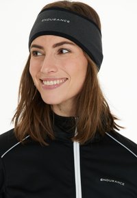 Mustavalkoinen hiusnauha, jossa on pehmeä pinta, etuosassa "ENDURANCE" -logo. Yhdistetty mustan vetoketjullisen takin kanssa.