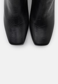 Zapatos negros de piel sintética con tacón cuadrado, patrón de cocodrilo texturizado, punta cuadrada y superficie lisa. Sin adornos visibles.