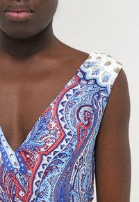 Robe sans manches avec un décolleté en V profond présentant un motif paisley bleu, rouge et blanc ; l'épaule a un accent blanc avec des motifs colorés.