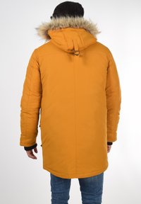 Narančasta parka jakna s kapuljačom od umjetnog krzna, dugim rukavima i ravnim krojem. Ima vidljiv zatvarač i elastične manžete.