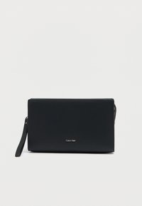 Pochette en cuir noir à texture lisse, fermeture éclair et bandoulière amovible. Présente un logo doré à l'avant.