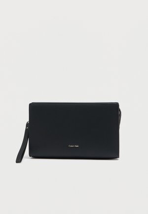 Pochette en cuir noir à texture lisse, fermeture éclair et bandoulière amovible. Présente un logo doré à l'avant.