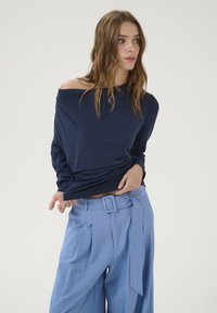 Marinblus med off-shoulder och långa ärmar, kombinerad med ljusbl�å, randiga vida byxor med bältad midja och sidoknytning.