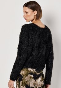 Schwarzer, samtig strukturierter Pullover mit weitem Ausschnitt, langen Ärmeln und cropped Passform, kombiniert mit einem Rock mit floralen Mustern.