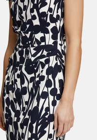 Robe à motif floral marine en tissu lisse et extensible ; présente un corsage ajusté et une jupe légèrement évasée avec un fond contrastant blanc.