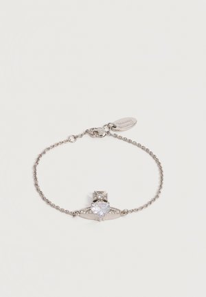 Bracelet chaîne en argent avec une pierre précieuse claire en forme de cœur en son centre et un petit détail en forme de croix, avec un fermoir mousqueton et une étiquette de marque.