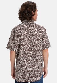 Korte mouw bruine shirt met een wit geometrisch en bloemmotief, gemaakt van lichte stof met een kraag en een ontspannen pasvorm.