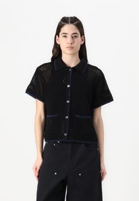 Black short-sleeve knit shirt with a collared neck, button front, and contrasting blue stitching. Features two front pockets.