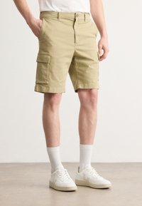 Khaki cargo shorts made of cotton, featuring side pockets, a zipper fly with a button closure, and rolled hem, paired with white socks and shoes.