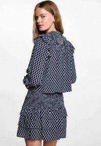 Svart och vit mönstrad klänning med volangaxlar, smockad bodice och flerlagad kjol. Lättviktig tyg med en mjuk textur.