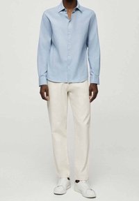 Chemise bleu clair à manches longues avec fermeture à boutons, associée à un pantalon blanc coupe droite et des baskets blanches. Design simple avec une texture lisse.