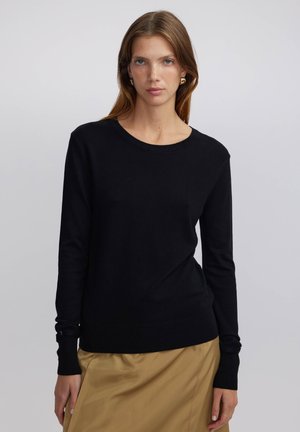 Černý pletený svetr s dlouhými rukávy, kulatým výstřihem a těsným střihem. Měkká textura, žebrované manžety a detaily lemu.