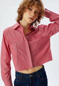 Rød- og hvidstribet cropped skjorte med krave, to brystlommer og knaplukning foran; parret med mørke denimjeans.