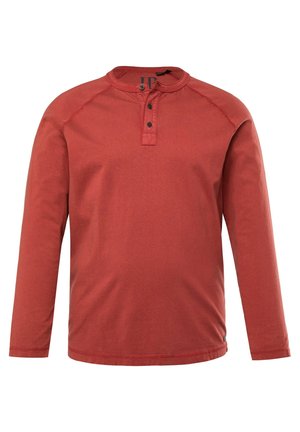 Chemise henley à manches longues en coton, de couleur rouge, dotée d'un col rond, d'une patte de boutonnage à trois boutons et de coutures contrastantes sur les épaules.