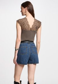 Brauner Spitzen-Top mit kurzen Ärmeln und V-Ausschnitt, kombiniert mit hochtaillierten Denim-Shorts. Die Shorts haben Gesäßtaschen und einen rohen Saum.