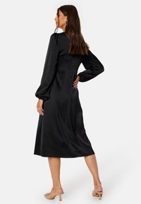 Černé saténové šaty s dlouhými balónovými rukávy a midi délkou, s přiléhavým korzetem a hladkým, lesklým povrchem.
