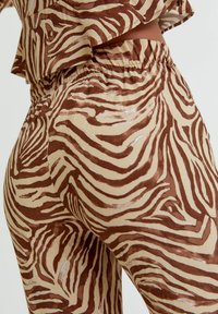 Gros plan sur un pantalon à rayures zèbres marron et beige avec une taille élastique et un haut assorti porté par une personne sur fond uni.