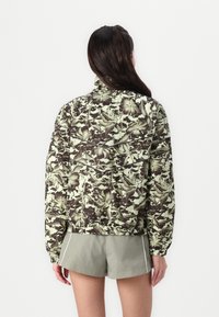 Floral-patterned jacket in green and brown tones, featuring a high collar, elastic cuffs, and a relaxed fit. Textured surface detail visible.