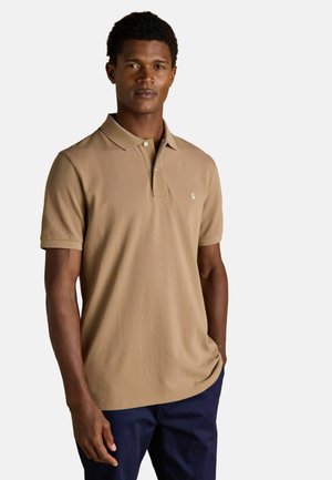 Tan polo shirt with a collar and three-button placket, featuring a small logo on the left chest. Short sleeves, soft texture.