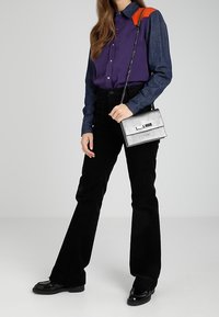 Czarne dzwony z sztruksu zestawione z fioletowo-dżinsową koszulą na guziki z pomarańczowym detalem na ramieniu. Niesie srebrną torebkę.