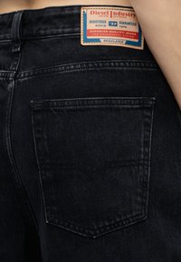 Μαύρο τζιν από denim, πίσω όψη που δείχνει μια δερμάτινη ετικέτα με την επωνυμία Diesel Industry πάνω από την δεξιά τσέπη.