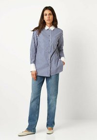 Blue and white striped button-up shirt with a white collar, paired with light blue straight-leg jeans and cream flats. Smooth fabric texture.