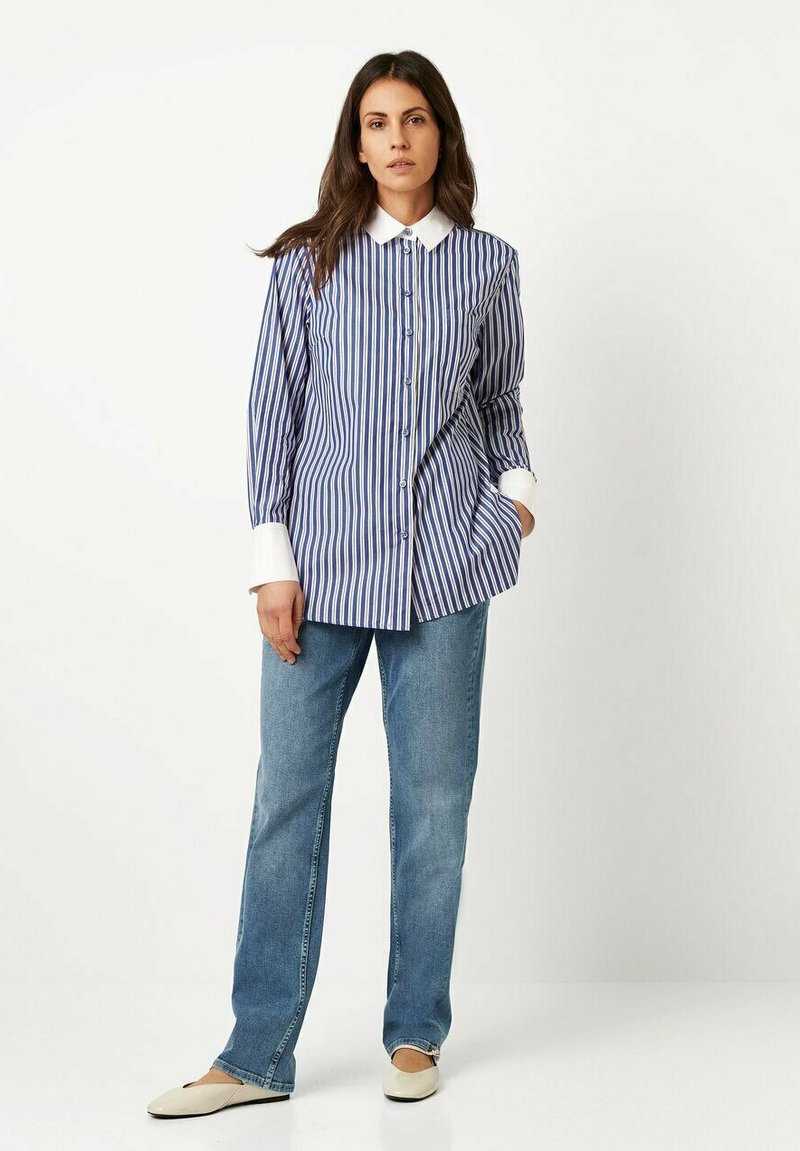 Blue and white striped button-up shirt with a white collar, paired with light blue straight-leg jeans and cream flats. Smooth fabric texture.