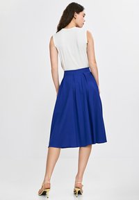 Niebieska plisowana spódnica z wysokim stanem, wykonana z gładkiego materiału. Noszona z białym bezrękawnym topem i żółtymi sandałami na obcasie.