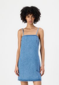 Sivuharmaa farkkutunika ohuilla säädettävillä olkaimilla, neliömäisellä pääntiellä ja revityillä helmalla. Tiukka malli, jossa on sileä pinta.