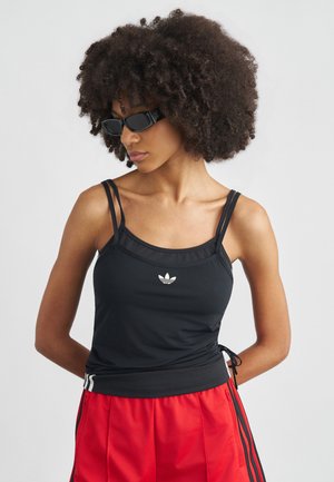 Débardeur de sport noir à fines bretelles, avec un logo blanc sur la poitrine et des côtés à cordon, assorti à un short rouge et des lunettes de soleil noires.