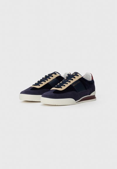 Un paio di sneakers lacciate blu navy e beige con suole bianche e il logo PS Paul Smith sui lati e sul tallone.