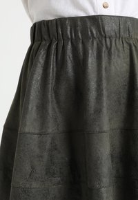 Gonna verde, strutturata, con vita arricciata e dettagli di cucitura orizzontale. Realizzata in un materiale sintetico lucido.