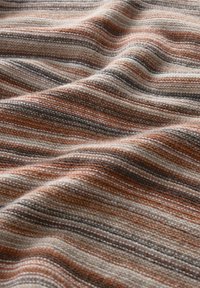 Tissu aux tons chauds, présentant des rayures alternées de beige, marron et rouille, avec une apparence tissée et texturée créant profondeur et fluidité.