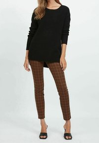 Schwarzer gerippter Pullover mit langen Ärmeln, kombiniert mit braunen karierten Slim-Fit-Hosen und schwarzen High Heels. Einfaches Design, lässiger Look.