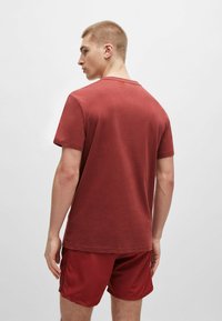 T-shirt in cotone color bordeaux con maniche corte, collo rotondo, vestibilità rilassata, mostrato di spalle. Abbinato a pantaloni corti bordeaux, texture liscia.
