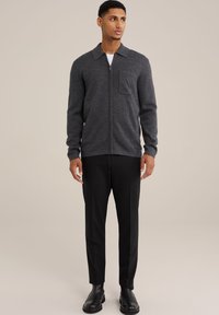 Grau zip-up Jacke mit Kragen und Fronttasche, kombiniert mit schwarzen maßgeschneiderten Hosen und schwarzen Knöchelstiefeln. Glatte Textur und taillierte Passform.