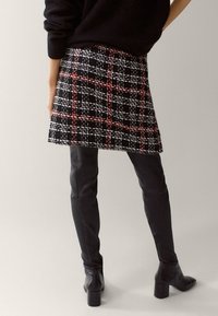 Zwarte geruite minirok met rode en witte accenten, gemaakt van gestructureerde stof; gecombineerd met leren laarzen tot boven de knie en een zwarte trui.