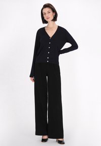 Cardigan navy con scollo a V, maniche lunghe e bottoni a perla, abbinato a pantaloni neri a gamba larga e tacchi neri. Tessuto dall'aspetto liscio.