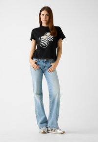 T-shirt nera corta con design grafico bianco sul davanti, abbinata a jeans a vita alta azzurri e scarpe da ginnastica argento.