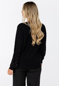 Zwarte trui met lange mouwen, versierd met verspreide versieringen op de mouwen. Gemaakt van een zachte breimateriaal, met een relaxte pasvorm.