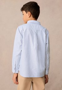 Világoskék-fehér csíkos hosszú ujjú ing sima tapintású anyagból; gombos gallérral és mandzsettával.