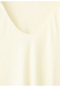 Tessuto color crema con trama testurizzata e un delicato motivo arricciato, con una scollatura ampia e arrotondata.