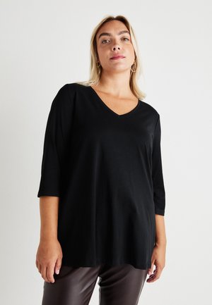 Top preto com decote em V e mangas três quartos, textura suave, ajuste relaxado, combinado com calças de imitação de couro castanhas. Design simples e versátil.