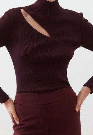Burgundy ribbed turtleneck-paita, jossa on epäsymmetrinen leikkaus ja pitkät hihat, yhdistettynä samanvärisiin korkeavyötäröisiin housuihin.