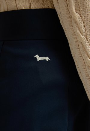 Tissu noir avec un petit chien teckel brodé en blanc à côté d'une manche beige en maille torsadée.