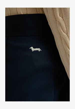 Black fabric with a small white embroidered dachshund dog next to a beige cable-knit sleeve.