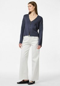 Cárdigan marino con cuello en V y botones en la parte delantera, combinado con pantalones vaqueros blancos de pierna ancha. Zapatos planos negros completan el conjunto. Textura suave.