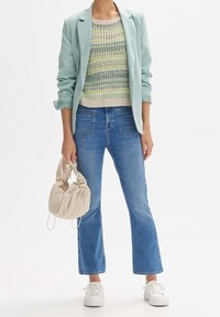 Blazer de menta claro sobre un suéter de punto multicolor. Jeans cortos azules, zapatillas blancas y un bolso de mano color crema.