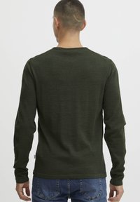 Chemise à manches longues verte en tissu doux, avec un col rond et une coupe ajustée. La vue de dos montre un design simple sans ornements.