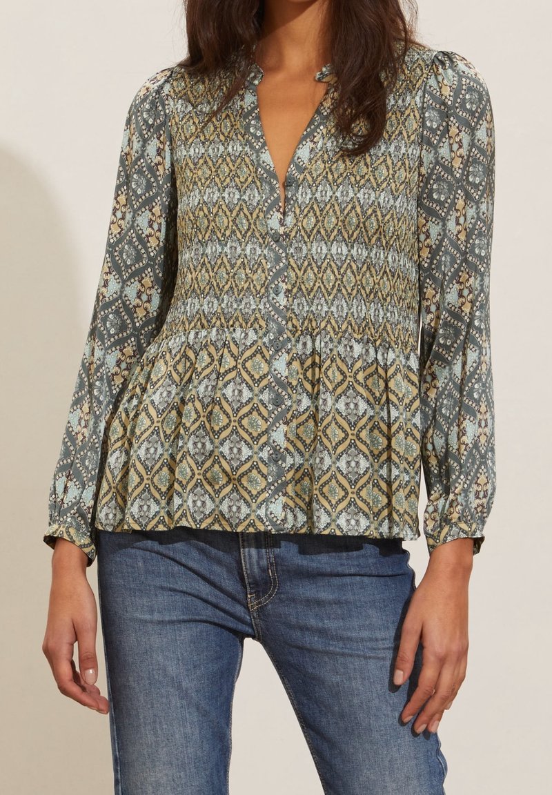Långärmad, mönstrad blus i teal, gul och kräm. Har en v-ringning, plisserad peplumslut och knäppning fram.